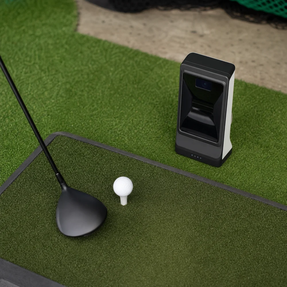 A golf launch monitor beside a golf ball on a practice mat.