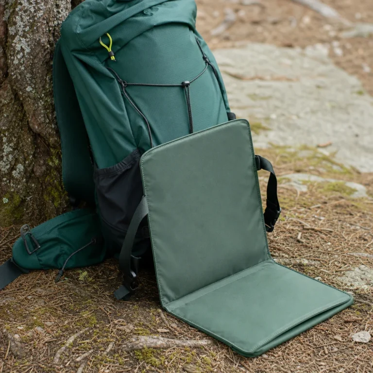 A compact trail seat next to a daypack on a trail surface