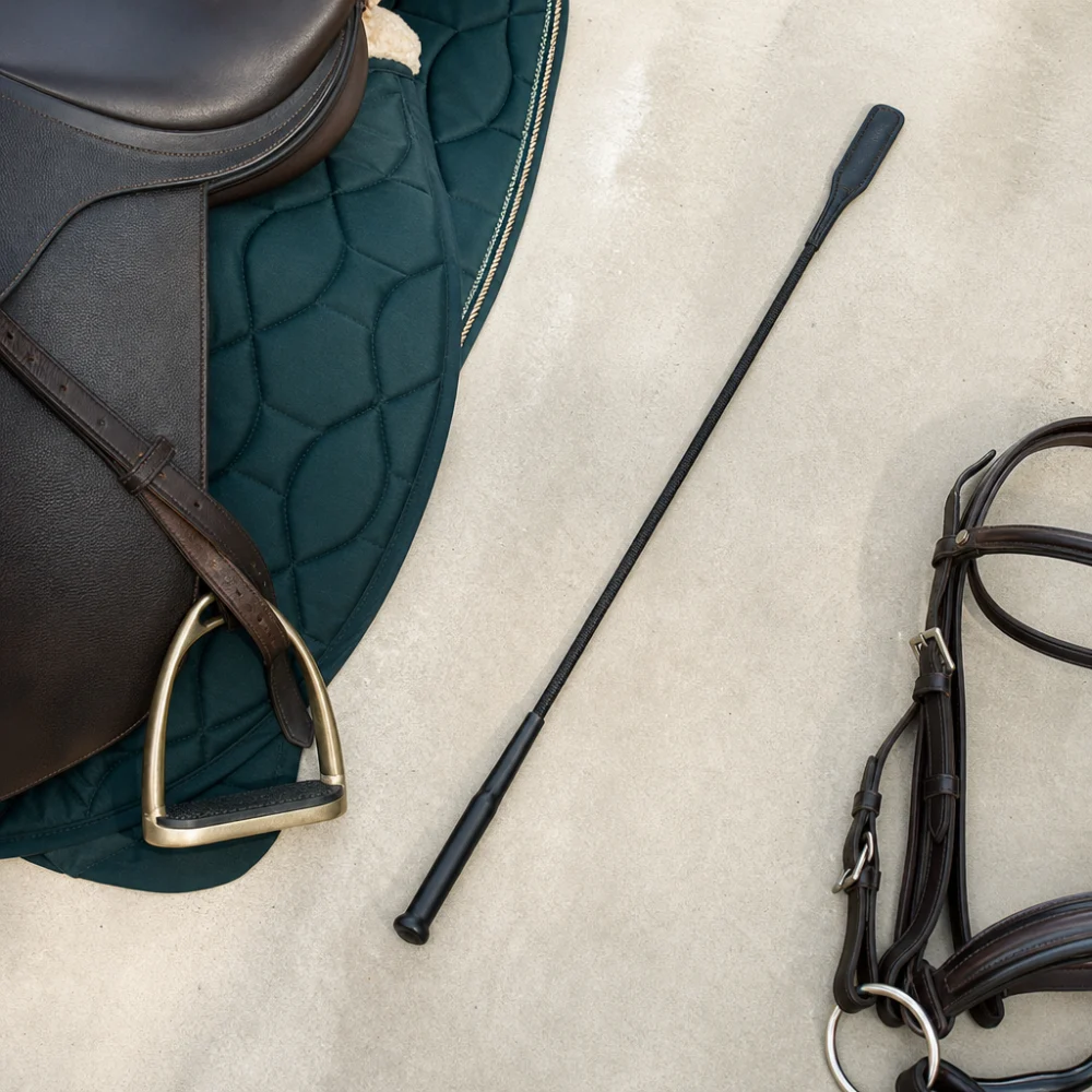 A riding whip displayed with equestrian tack on a neutral background.