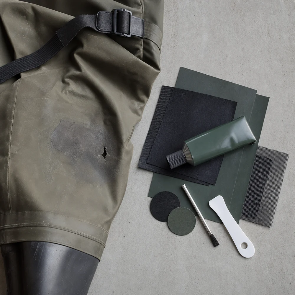 Generic wader repair kit materials arranged beside fishing waders on a neutral surface.
